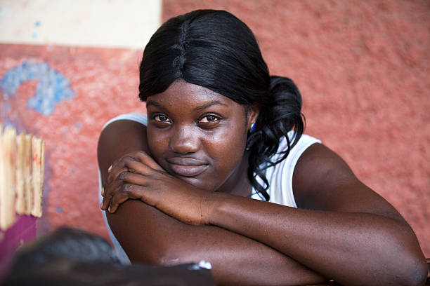 Falmouth, Jamaica, August 28, 2013: Young Jamaican woman, sitting in front of a red wall on the street, with a slight smile